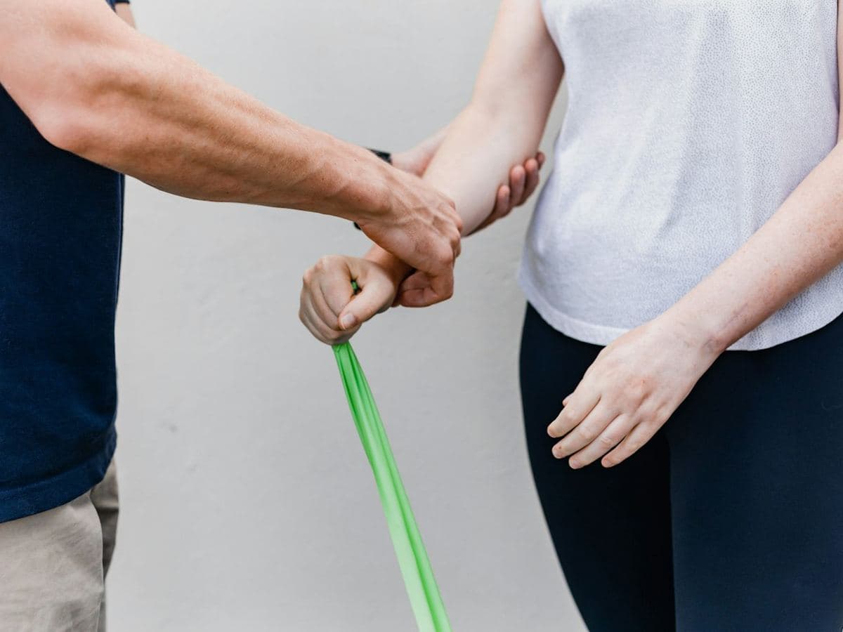 Paciente hace ejercicio de rehabilitación con una liga y apoyo del fisioterapeuta